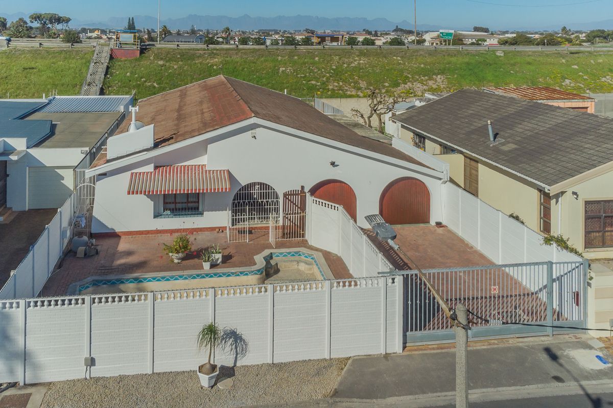 Aerial view of a residential property featuring a swimming pool, paved driveway, secure perimeter walling, and arched garage access.