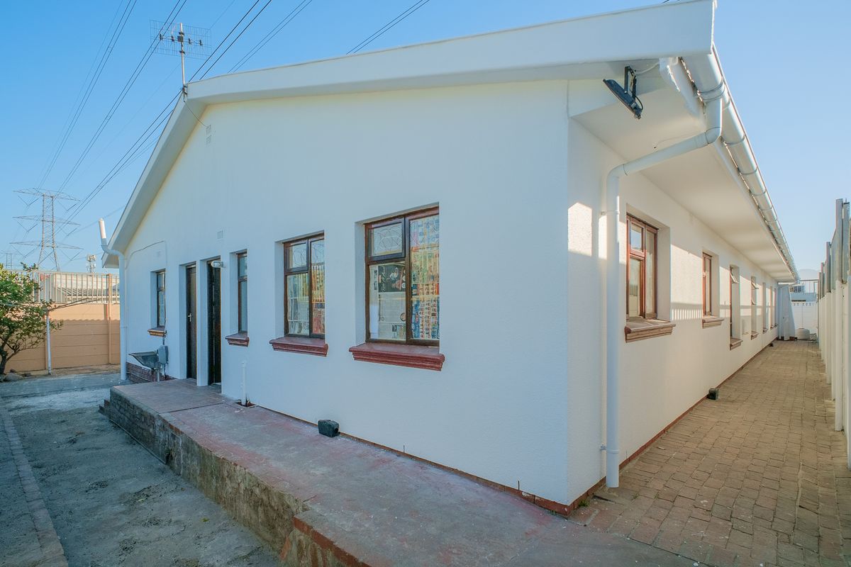 A view of the rear exterior of the house featuring a paved walkway, white rendered walls, and functional guttering systems.