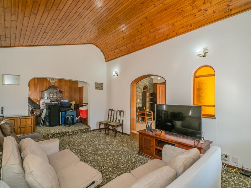 Spacious living room featuring a vaulted timber ceiling, arched architectural details, and an arched window, offering a traditional layout with connected living spaces.