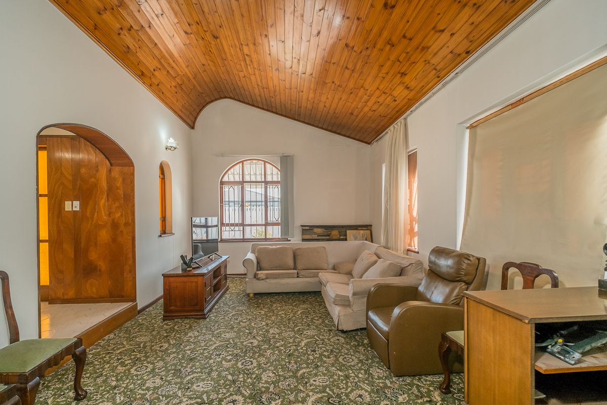 Spacious living room featuring a high vaulted timber ceiling, arched architectural details, and large windows providing natural light.