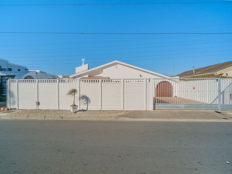 Front exterior view of the property featuring a secure perimeter wall, sliding gate, and paved driveway access.
