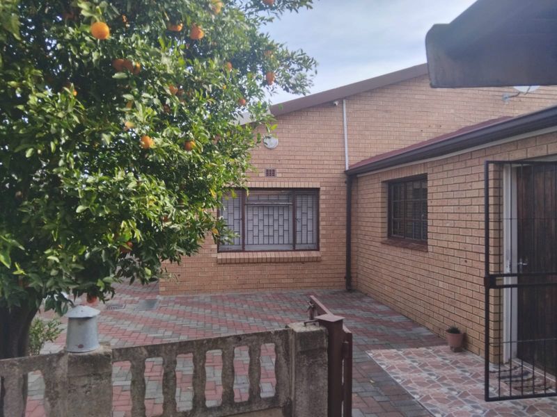 A rear exterior view of the house featuring a face brick facade, paved courtyard area, and secure window bars.
