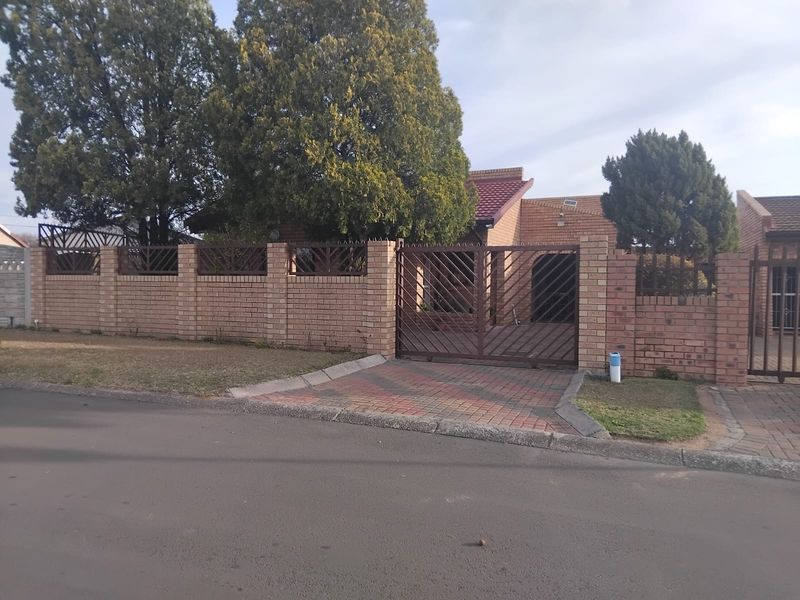 Front view of a face brick house featuring a paved driveway, secure metal gate, and perimeter boundary wall with security spikes.