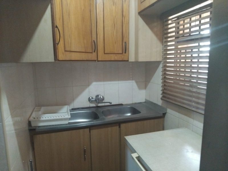 A functional scullery area featuring a double stainless steel sink, tiled splashback, and wooden cabinetry with integrated storage.