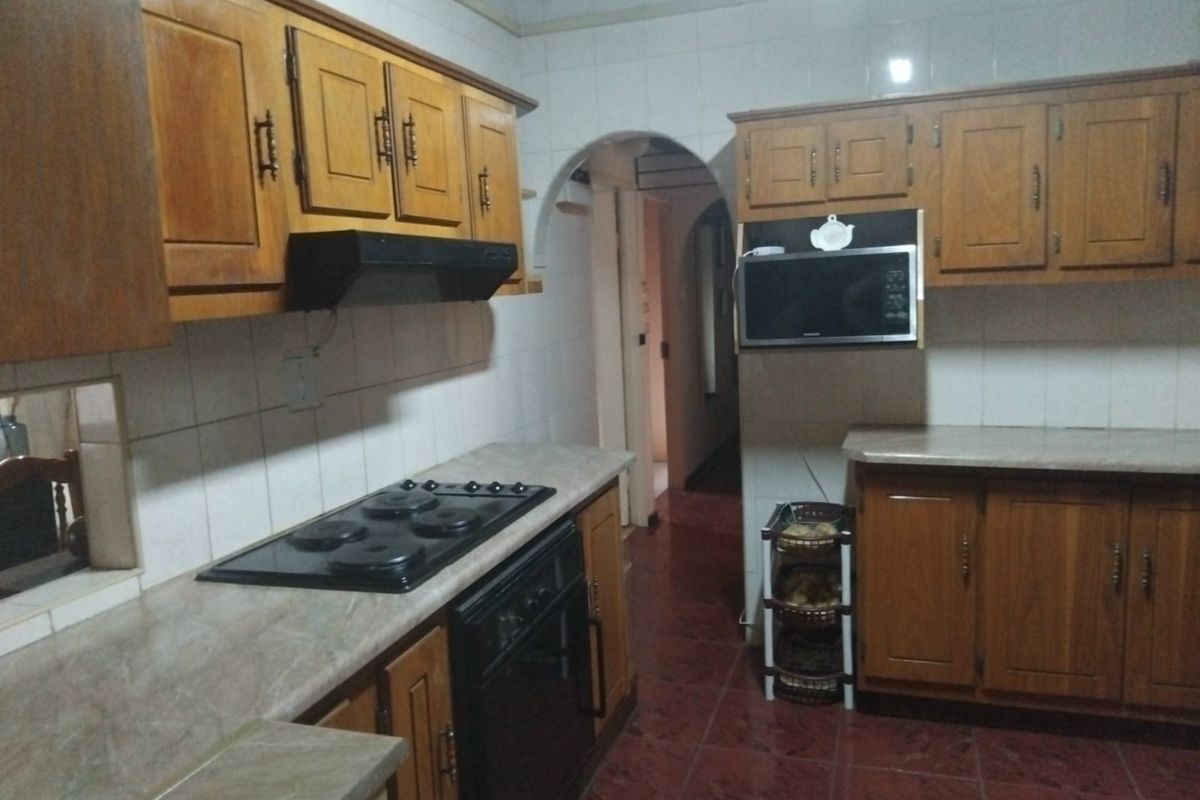 A functional kitchen featuring traditional wooden cabinetry, built-in appliances including an oven and hob, and tiled finishes throughout.