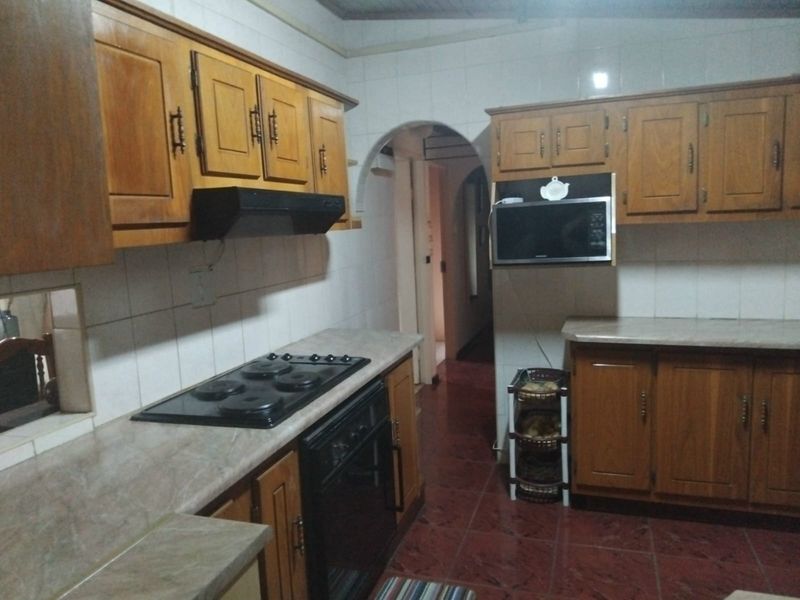 A functional kitchen featuring traditional wooden cabinetry, built-in appliances including an oven and hob, and tiled finishes throughout.