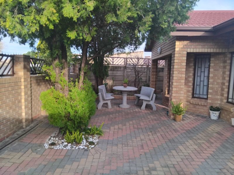 A paved outdoor patio area featuring facebrick construction, secure window bars, and a private garden setting with established trees.