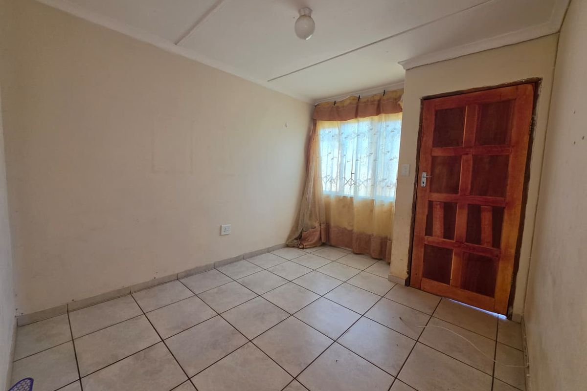 An empty bedroom featuring tiled flooring, a wooden door, and a simple ceiling light fixture, ready for renovation or staging.