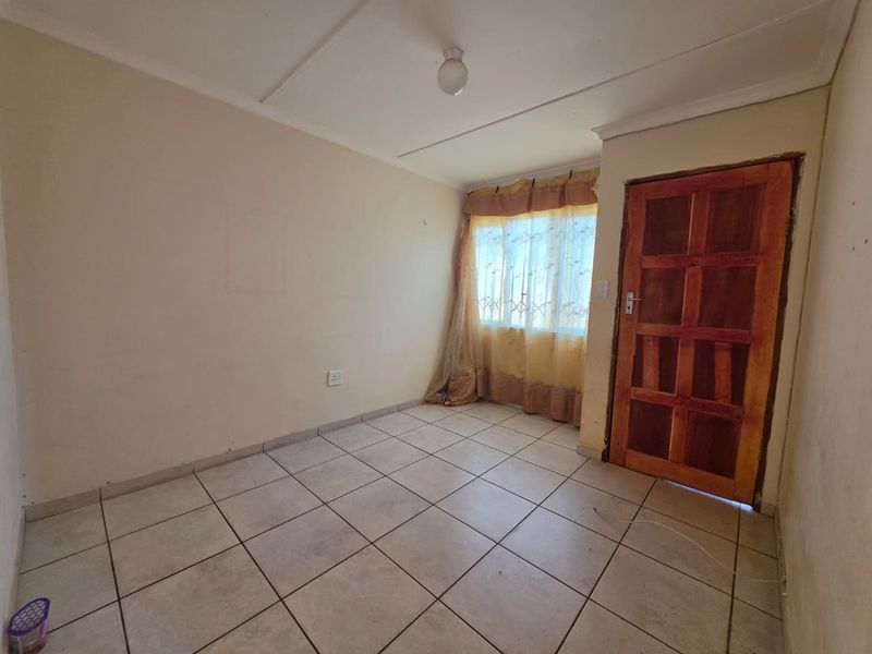 An empty bedroom featuring tiled flooring, a wooden door, and a simple ceiling light fixture, ready for renovation or staging.