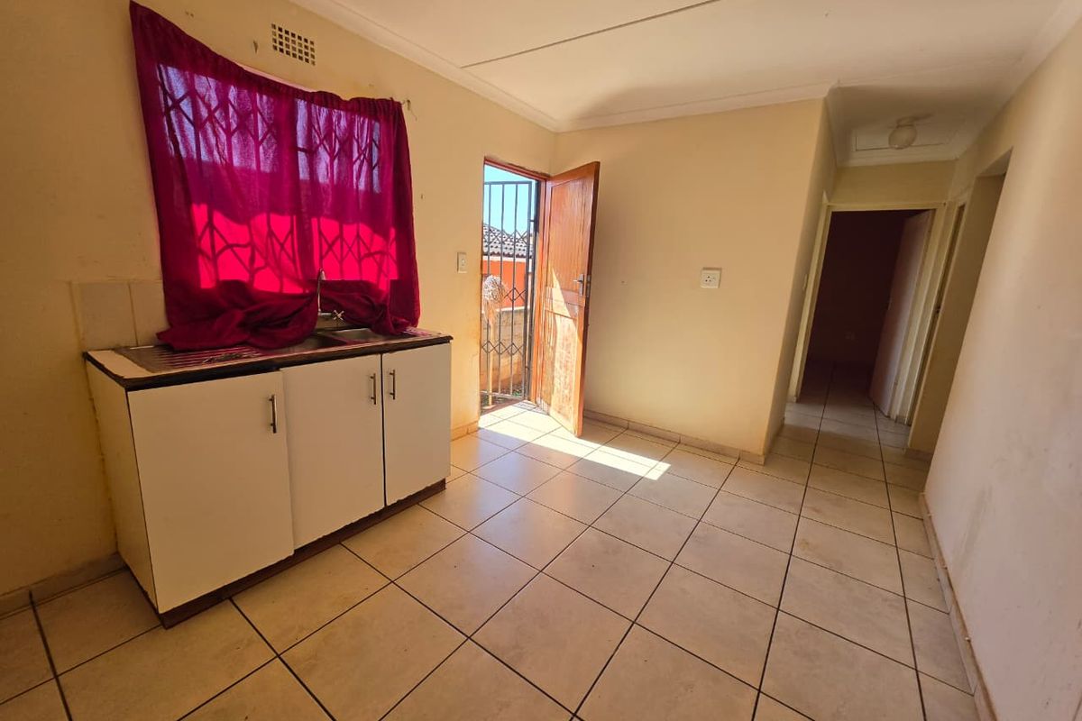 A compact kitchen area featuring basic base cabinetry, a sink, tiled flooring, and direct access to an exterior space via a security gate.