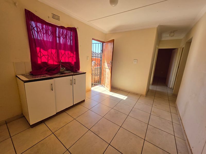 A compact kitchen area featuring basic base cabinetry, a sink, tiled flooring, and direct access to an exterior space via a security gate.