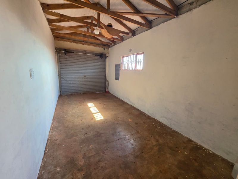 A spacious, empty garage featuring exposed timber roof trusses, a roller shutter door, and a concrete floor, offering potential for storage or workshop use.