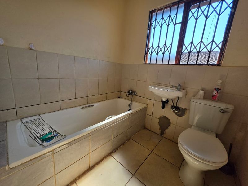 A functional bathroom featuring a built-in bathtub, wall-mounted basin, and toilet, requiring cosmetic updates and repairs to wall tiling and finishes.