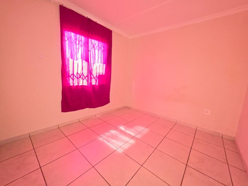 An empty bedroom featuring tiled flooring and a window fitted with a security gate.