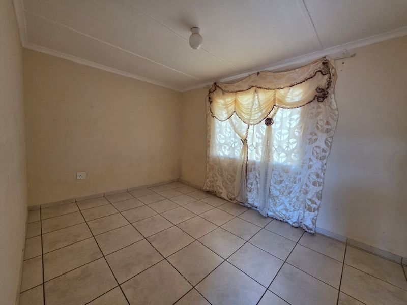 An empty bedroom featuring neutral tiled flooring and a single window, providing a blank canvas for potential interior design updates.