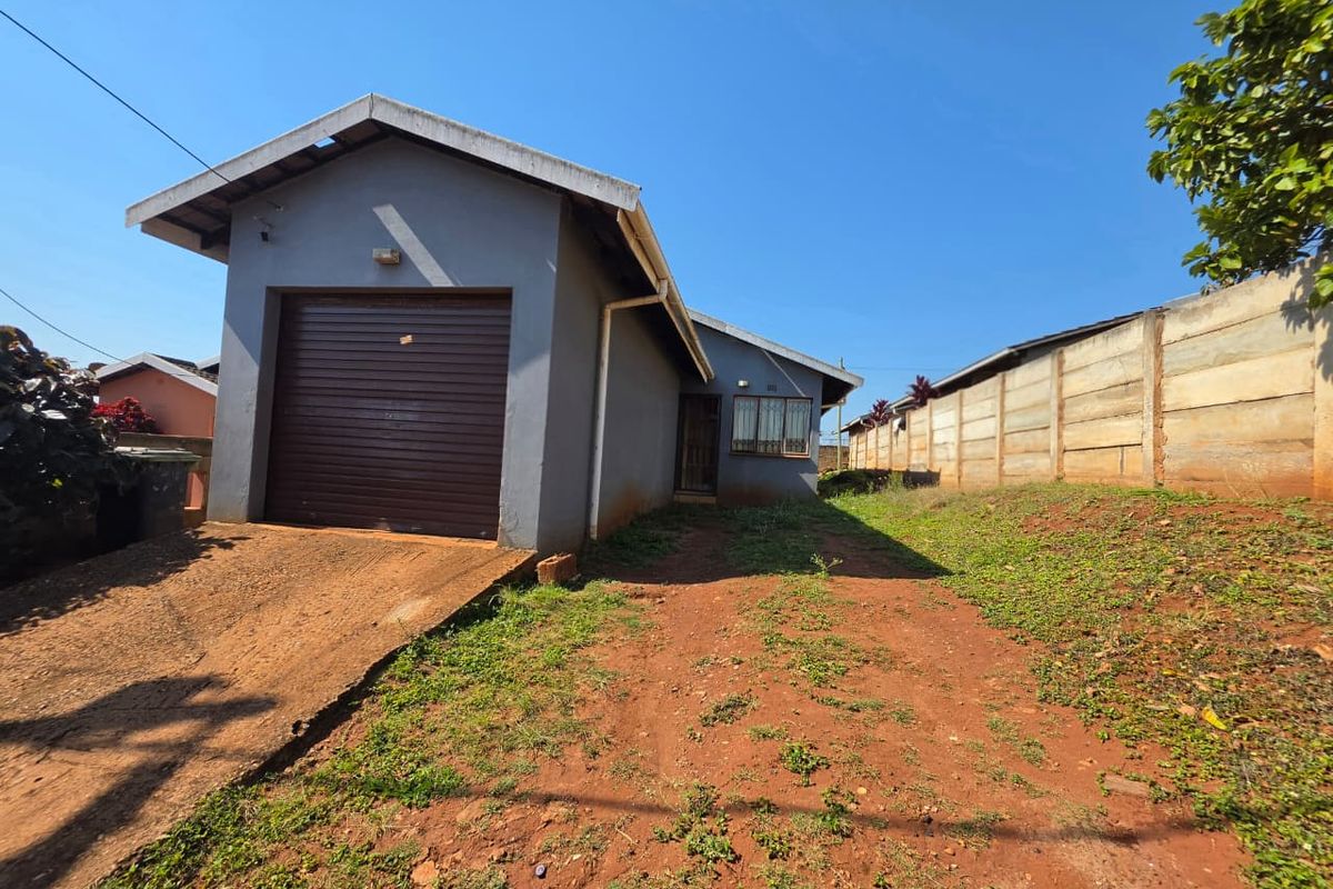 Front view of a detached house featuring a single roller garage door, concrete driveway, and a precast concrete boundary wall on a large plot.