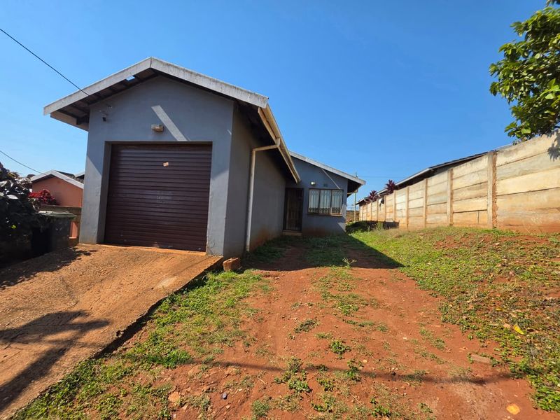 Front view of a detached house featuring a single roller garage door, concrete driveway, and a precast concrete boundary wall on a large plot.