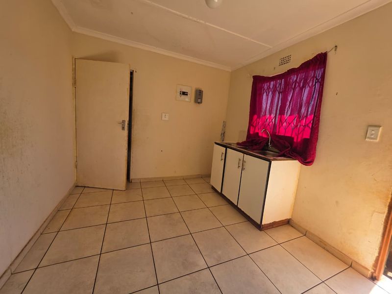 A compact, empty kitchen area featuring tiled flooring, basic base cabinetry with a sink, and a security gate over the window.