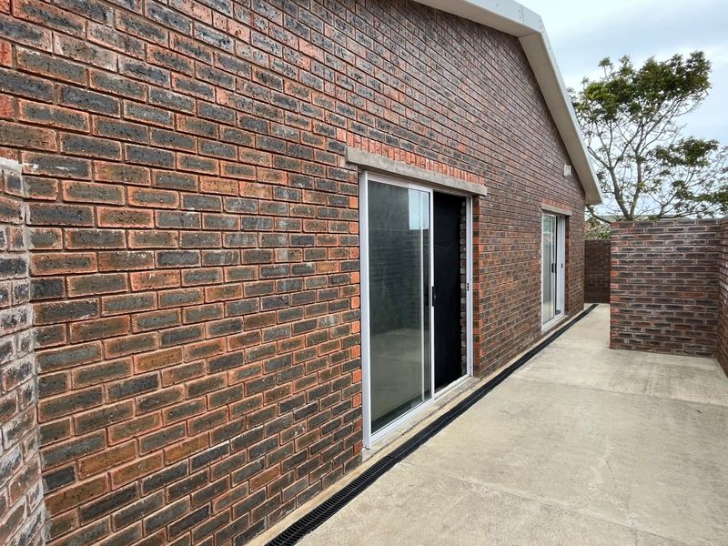 A clean rear exterior view featuring a face brick facade, concrete patio area, and modern sliding glass doors with integrated drainage.