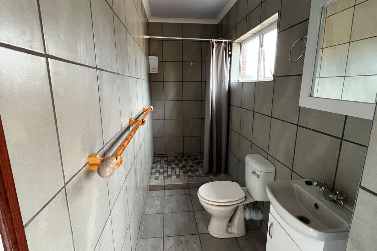 A functional bathroom featuring full-height wall tiling, a shower area with curtain, a standard toilet, and a vanity basin.