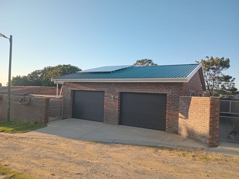 A detached double garage featuring face brick construction, roller doors, and a metal roof equipped with solar panels, set behind a perimeter wall.
