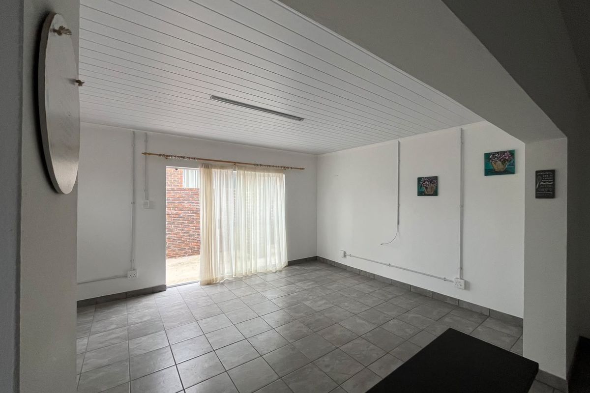 An empty living area featuring tiled flooring, a tongue and groove ceiling, and a sliding glass door providing access to the exterior.