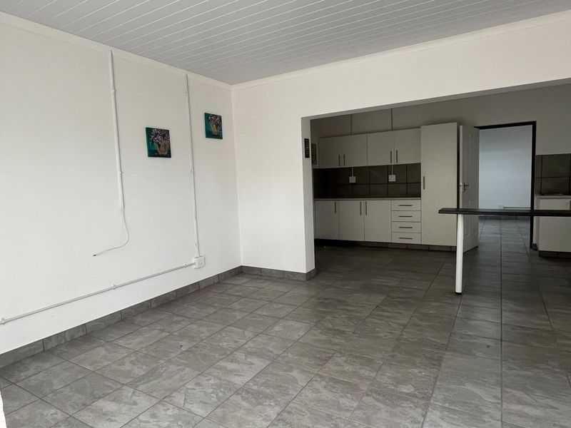 Open plan living area featuring tiled flooring and a functional kitchen with built-in cabinetry and a breakfast bar.