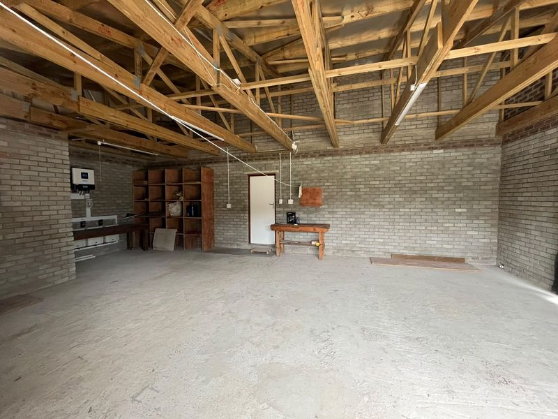 Spacious garage featuring exposed timber roof trusses, raw brick walls, and a concrete floor, suitable for storage or workshop use.