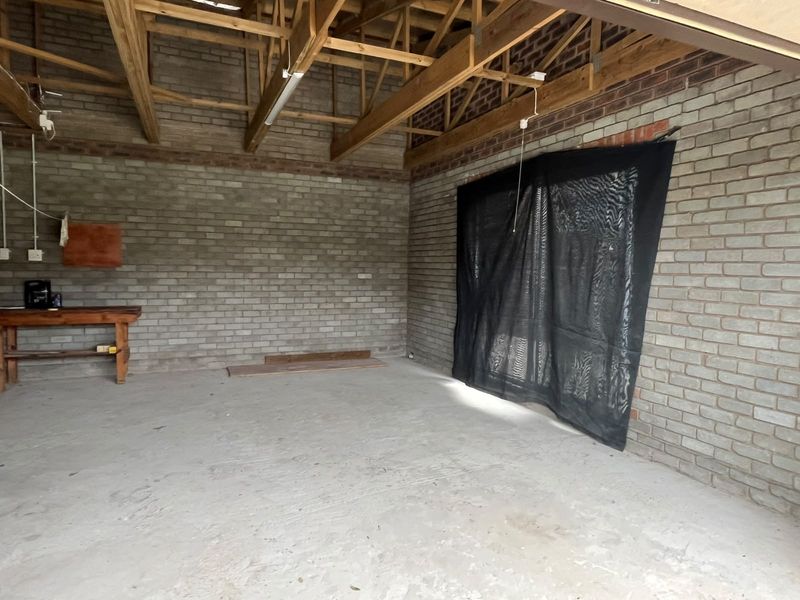 An unfinished garage space featuring exposed timber roof trusses, face brick walls, and a raw concrete floor, offering potential for workshop or storage use.