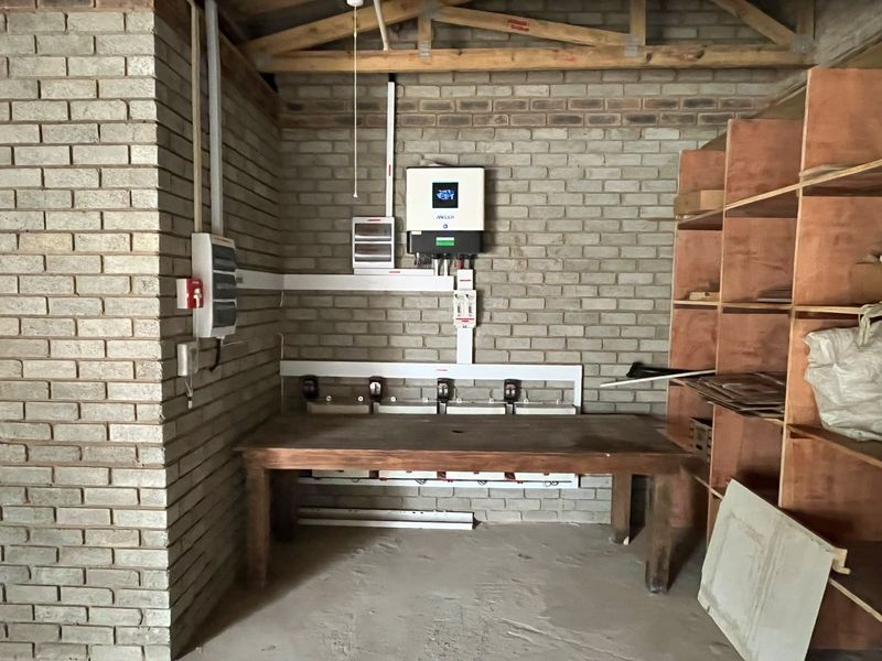 A functional utility space featuring exposed brick walls, timber roof trusses, and a wall-mounted inverter system with electrical distribution board.