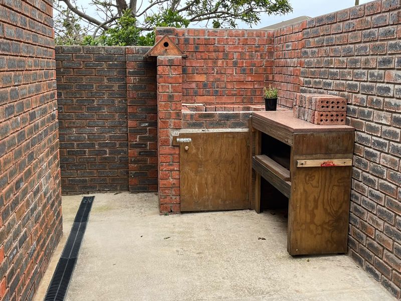 Outdoor patio area featuring a built-in brick braai, concrete flooring, and a functional drainage channel, enclosed by private brick boundary walls.