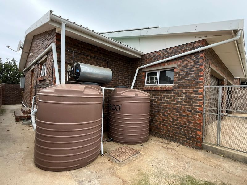 Rear exterior view showing brick facade, concrete paving, and installed water storage tanks with an external electric geyser unit.