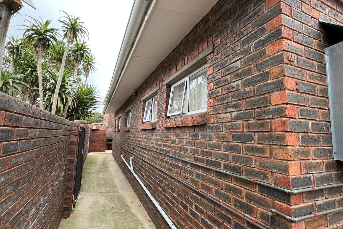 A side exterior view of the property featuring face brick walls, concrete pathways, and functional casement windows.
