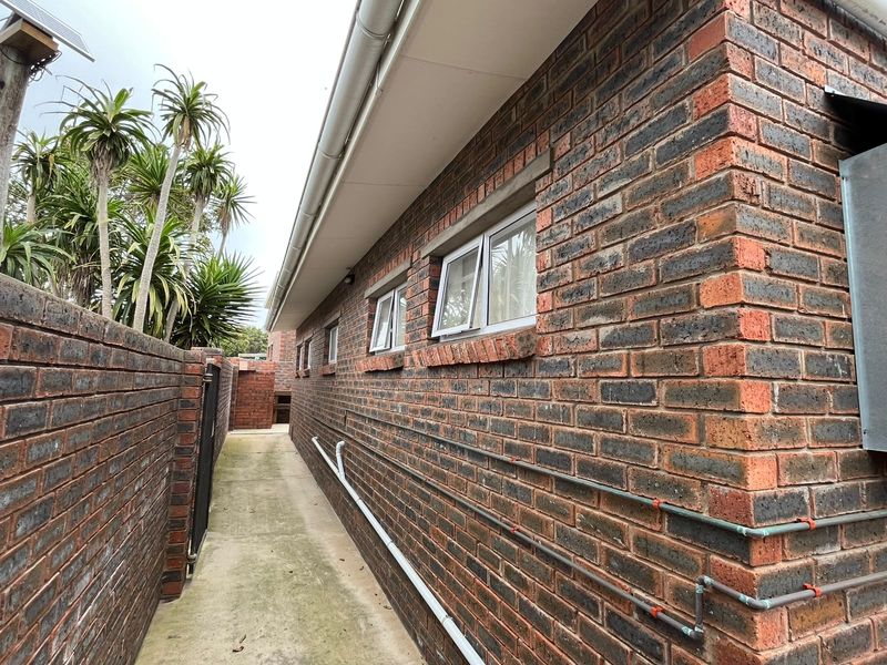 A side exterior view of the property featuring face brick walls, concrete pathways, and functional casement windows.