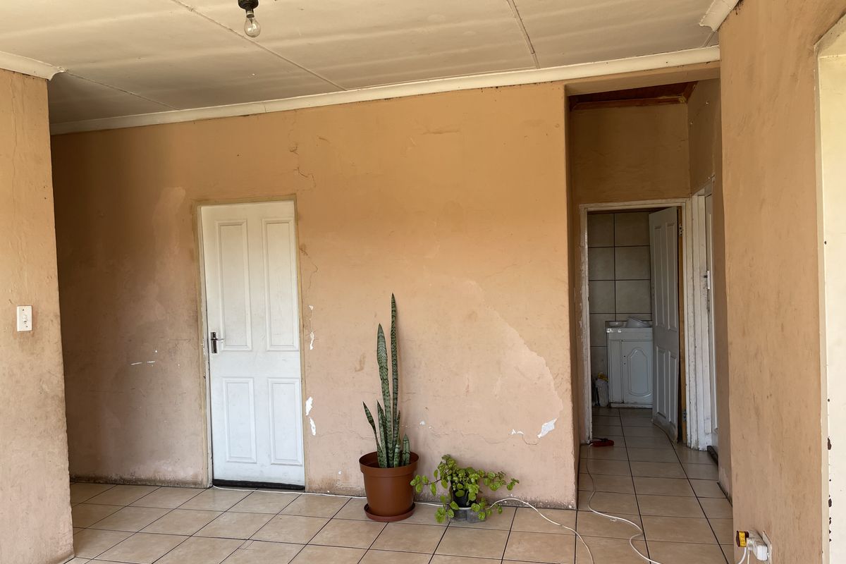 An empty living area featuring ceramic floor tiles, requiring cosmetic updates including wall repairs and ceiling maintenance.