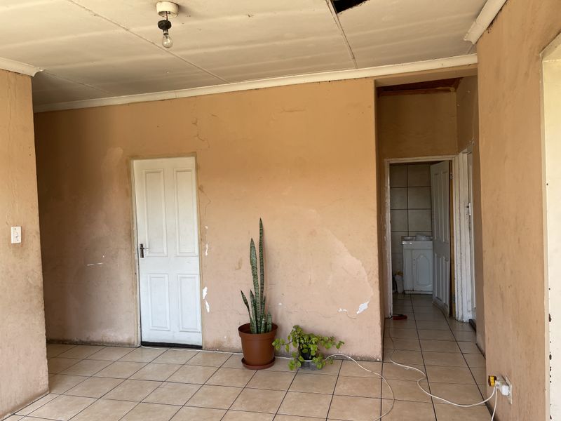 An empty living area featuring ceramic floor tiles, requiring cosmetic updates including wall repairs and ceiling maintenance.
