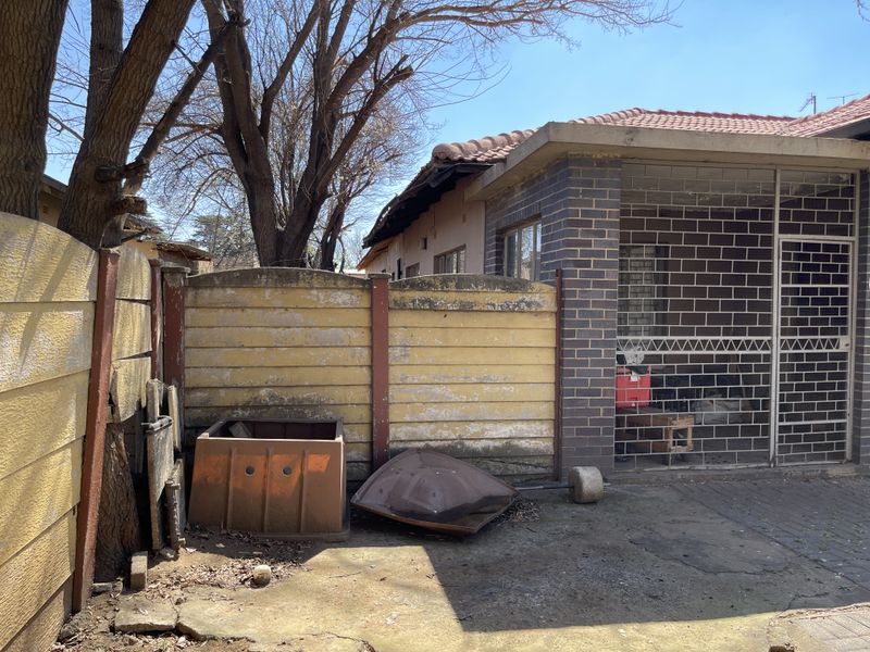Rear exterior view showing a paved patio area, brick building facade, and a weathered precast concrete boundary wall.