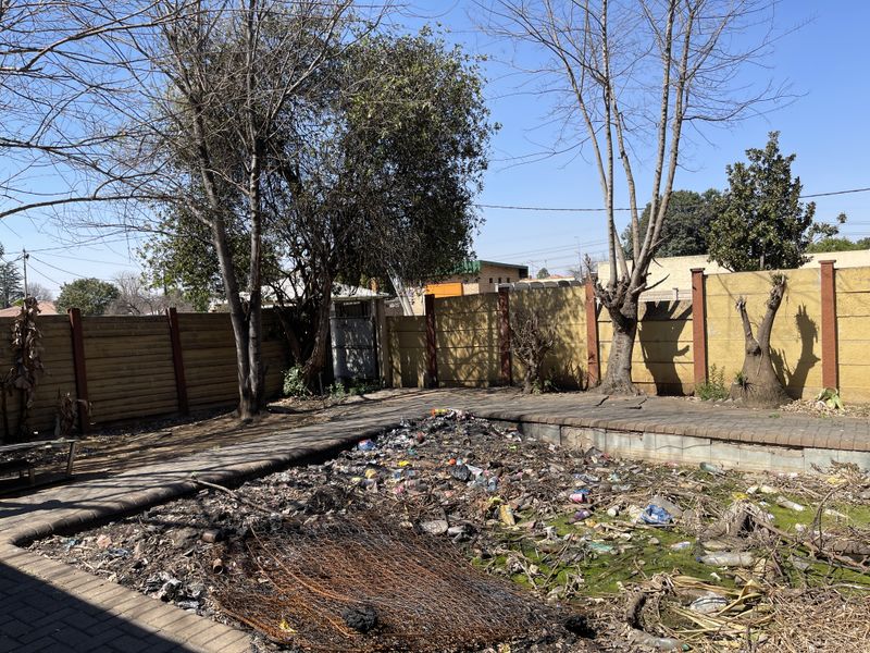 Outdoor pool area featuring a paved surround and boundary wall, currently in a state of severe neglect with significant debris accumulation.