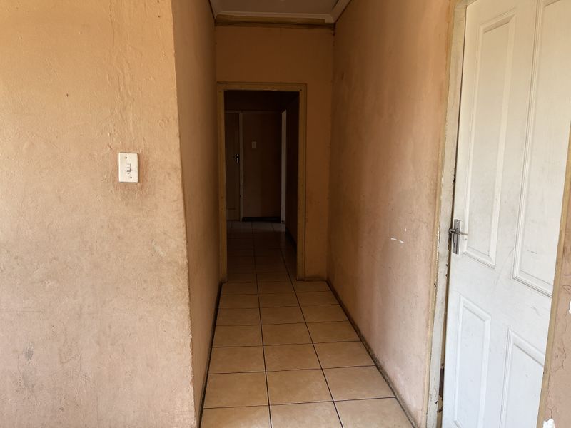 A vacant interior hallway featuring tiled flooring and plain wall finishes, providing access to adjacent rooms within the property.
