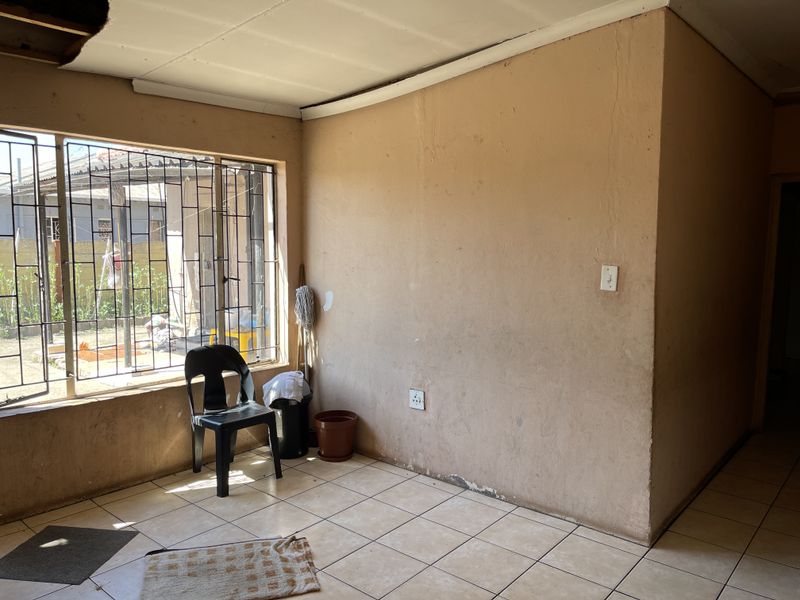 A vacant living area featuring tiled flooring, large windows with security bars, and plain walls in need of cosmetic attention.