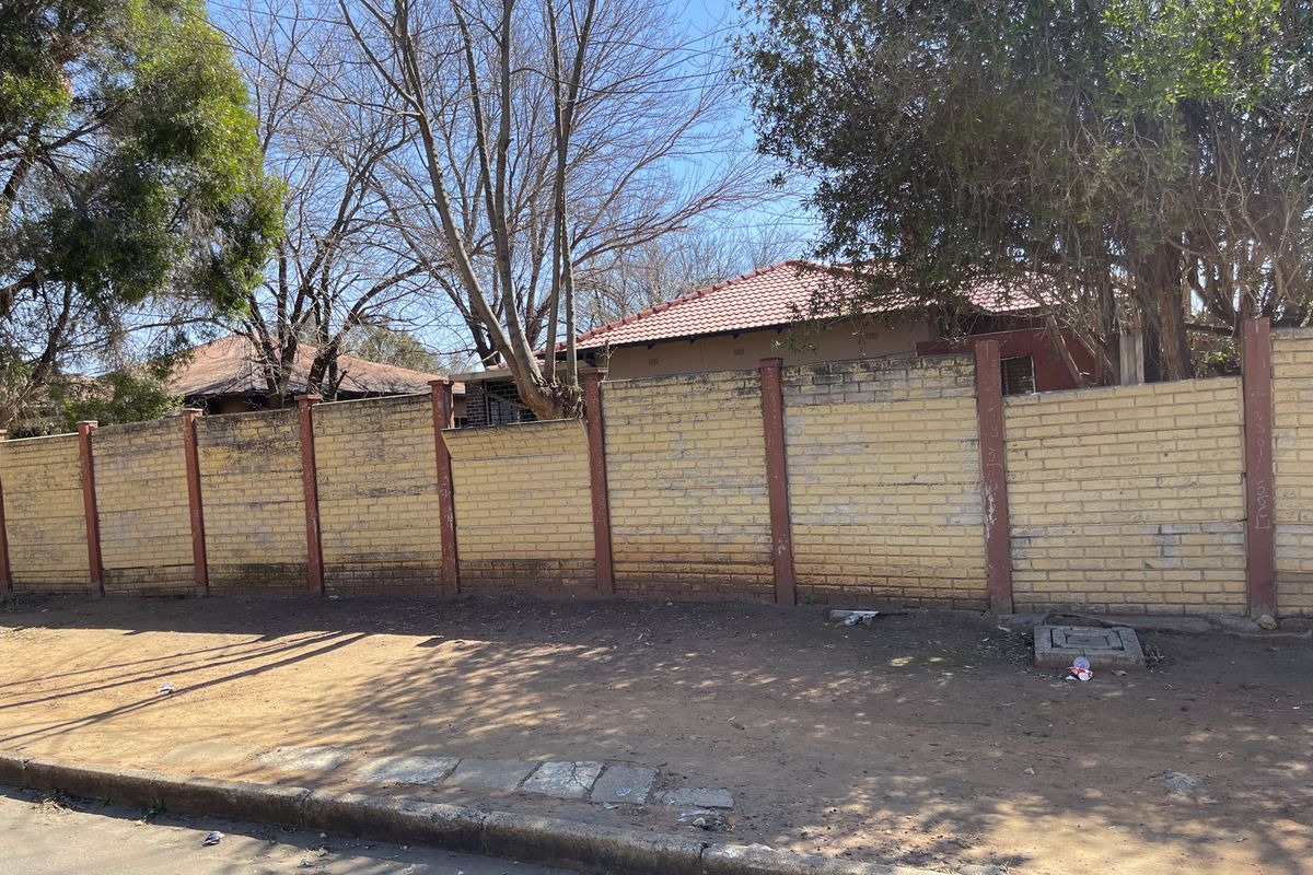 Street view of the property showing a weathered brick boundary wall with concrete pillars and a glimpse of the tiled roof structure.