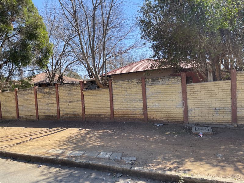 Street view of the property showing a weathered brick boundary wall with concrete pillars and a glimpse of the tiled roof structure.