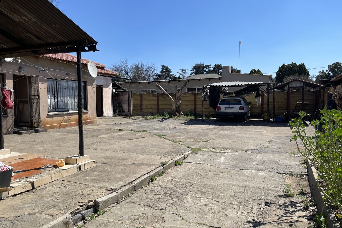 Rear exterior area featuring a large concrete driveway, a carport, and a covered patio attached to the main dwelling.