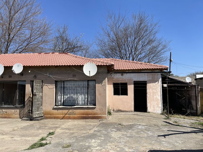Front elevation of a single-story house featuring a tiled roof, security bars on windows, and a concrete driveway in need of maintenance.