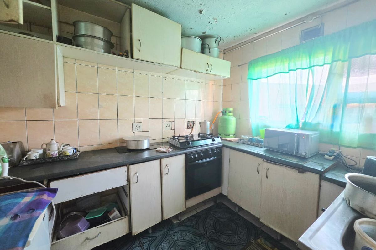 A dated kitchen featuring built-in cabinetry, a gas stove, and tiled backsplash, currently requiring significant renovation and cosmetic updates to improve functionality and aesthetic appeal.