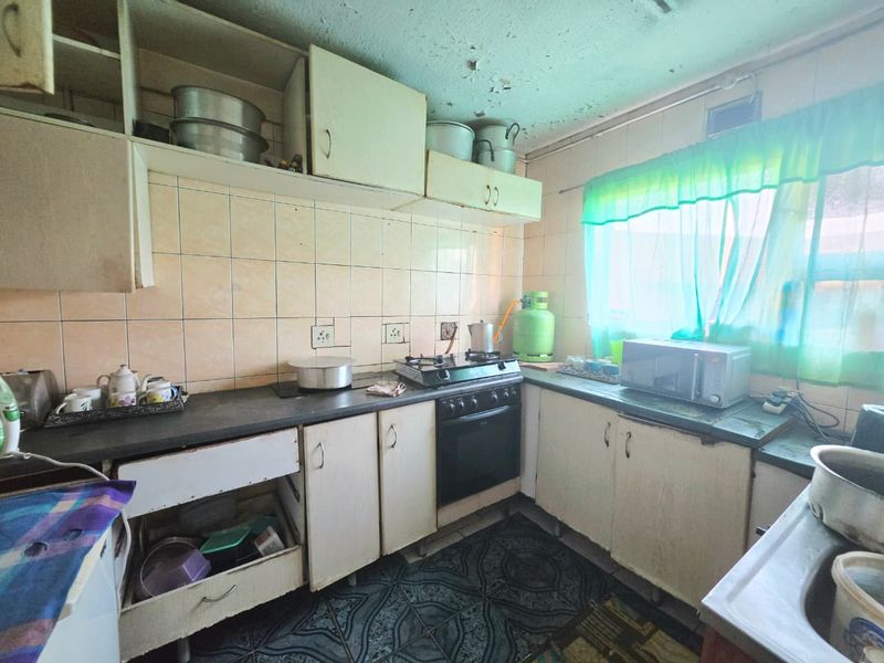 A dated kitchen featuring built-in cabinetry, a gas stove, and tiled backsplash, currently requiring significant renovation and cosmetic updates to improve functionality and aesthetic appeal.