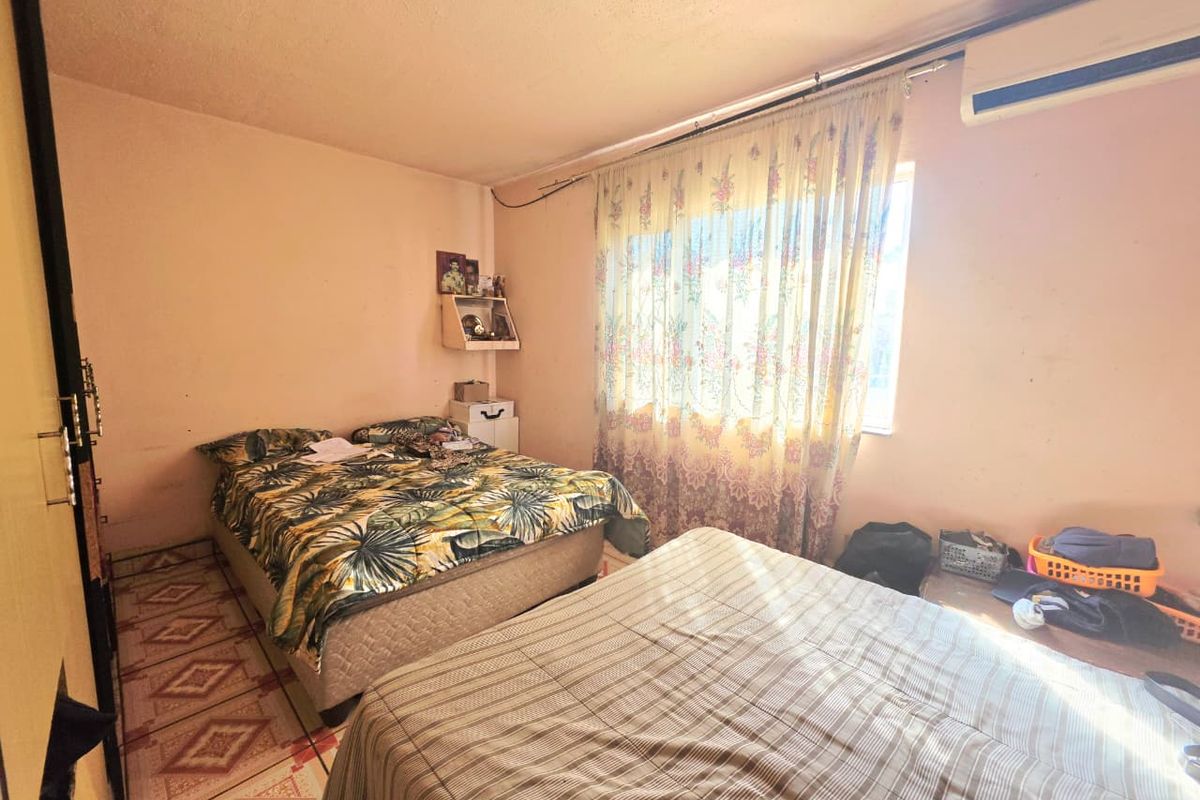 A bedroom featuring tiled flooring, a wall-mounted air conditioning unit, and built-in storage, requiring cosmetic updates to improve its overall condition.
