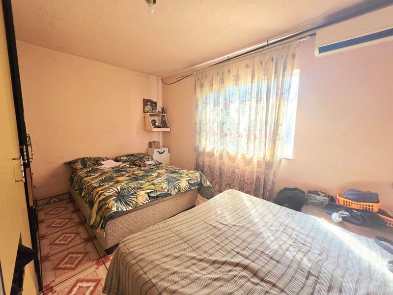A bedroom featuring tiled flooring, a wall-mounted air conditioning unit, and built-in storage, requiring cosmetic updates to improve its overall condition.