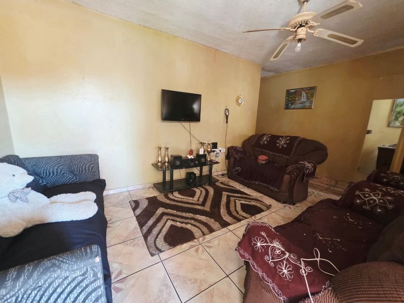 A living room featuring tiled flooring and a ceiling fan, currently showing signs of wear on the wall finishes.