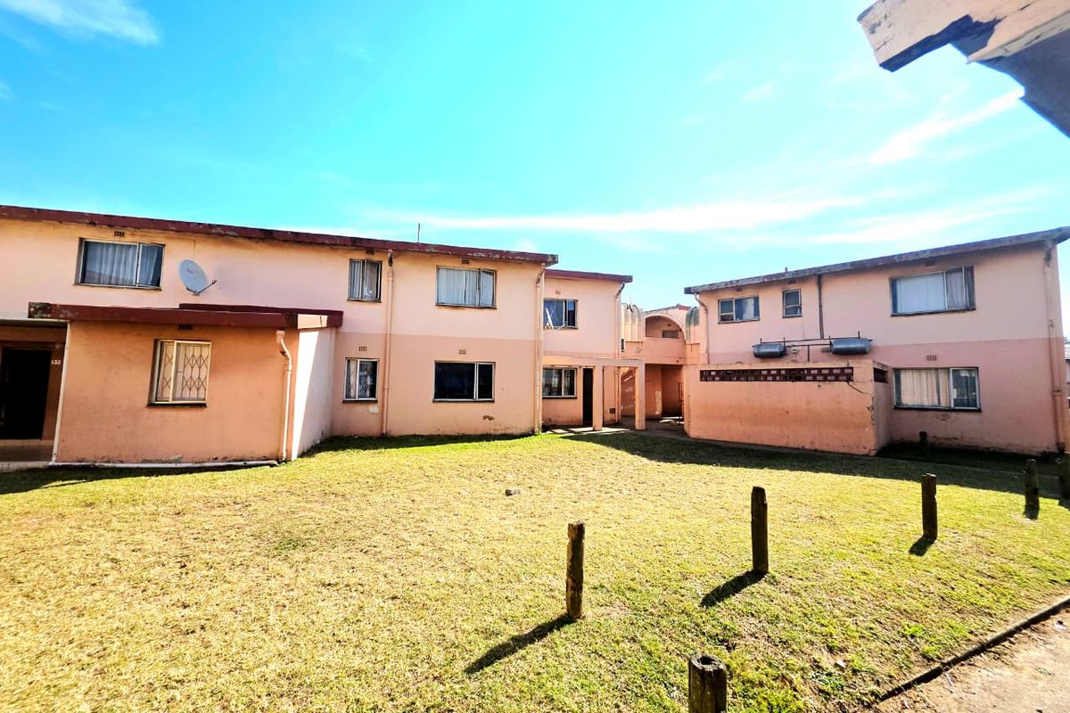 Rear view of a multi-unit apartment complex featuring a shared lawn area, weathered exterior walls, and security bars on windows.